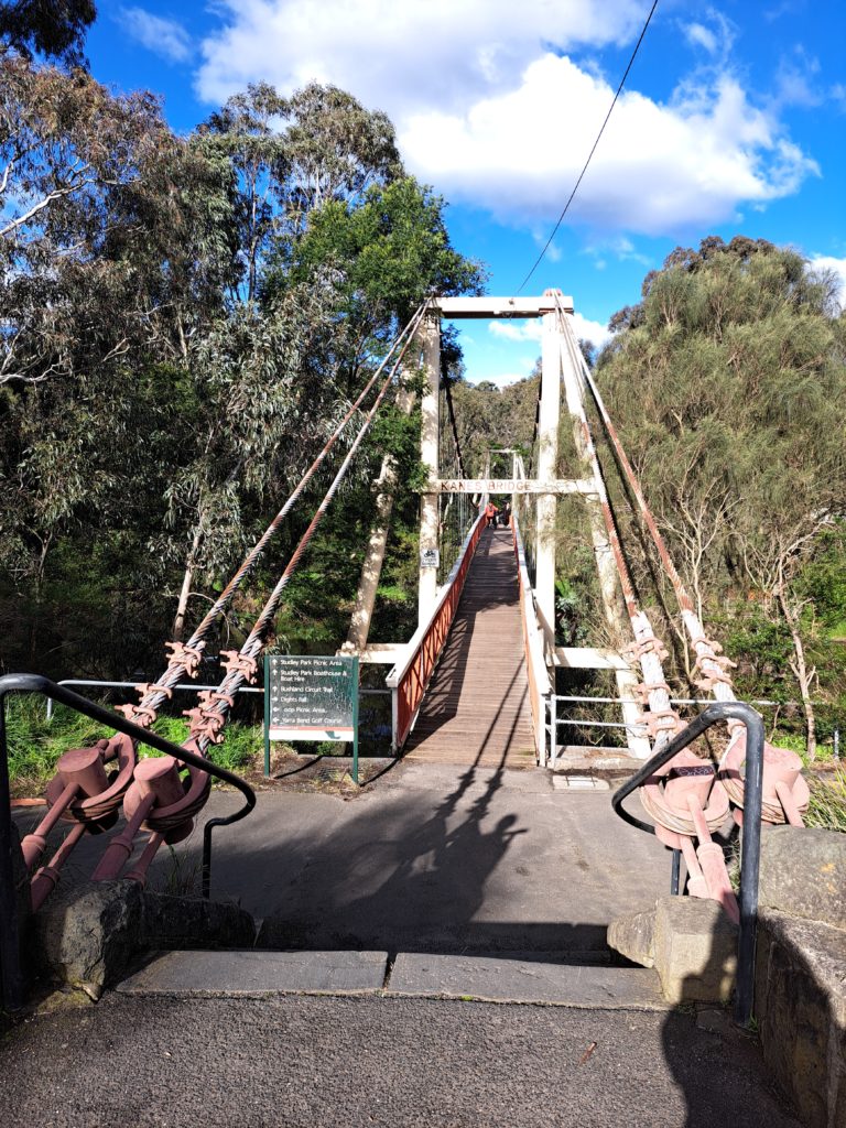 Kane's Bridge on the Yarra Road Side. Its a beautiful wooden bridge with faded red and white paint.