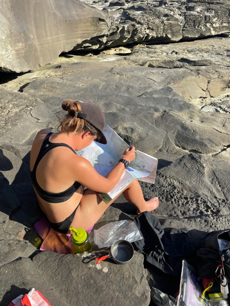 Woman reading a map on the warm rocks in the sun.