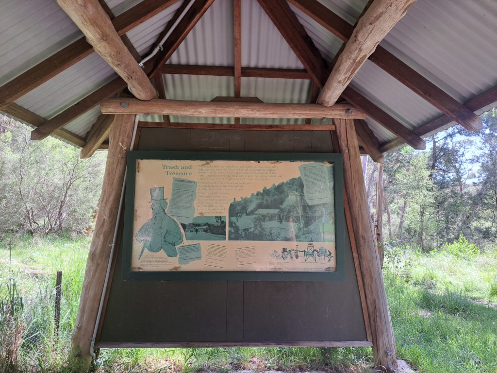 Picture underneath a shelter made of logs and corrugated iron sheets. On the wall of the shelter is an informative sign about the history of the area.